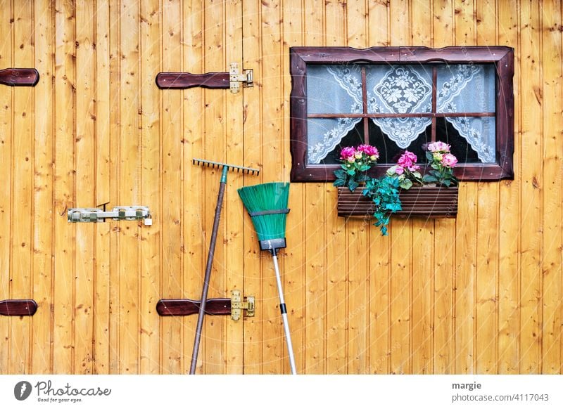 Eine Gartenhütte mit Fenster, Gardine,  Blumenkasten, davor angelehnt Besen und Rechen Gartenarbeit Gardiene Haus Tag Arbeit & Erwerbstätigkeit Gärtner Werkzeug