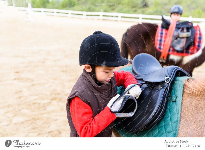 Junge stellt Steigbügel am Sattel ein ausrichten Ponys Reiterin Schule Arena Dressur Jockey Kind Lektion Pferderücken Sattelkammer Unterlage befestigen