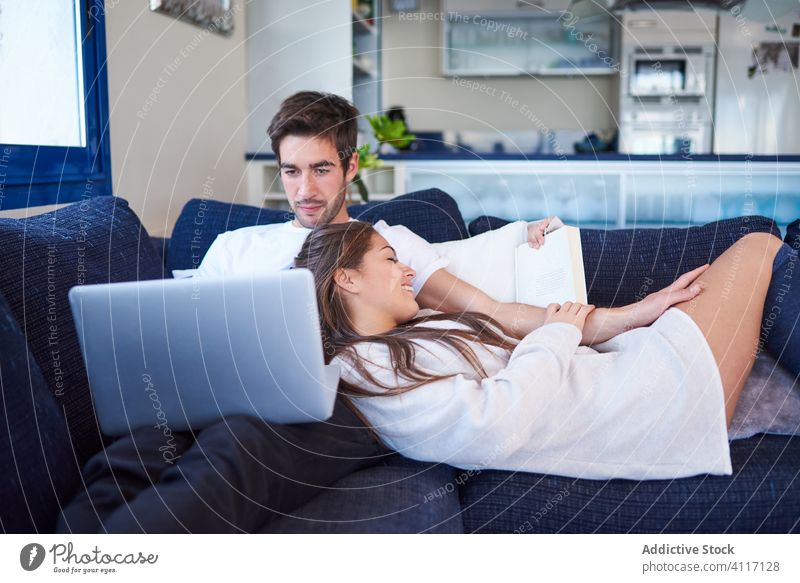 Junges Paar ruht sich zu Hause auf gemütlichem Sofa aus heimwärts Zusammensein ruhen Buch Laptop benutzend lesen jung Partnerschaft Ehemann Liege Gerät