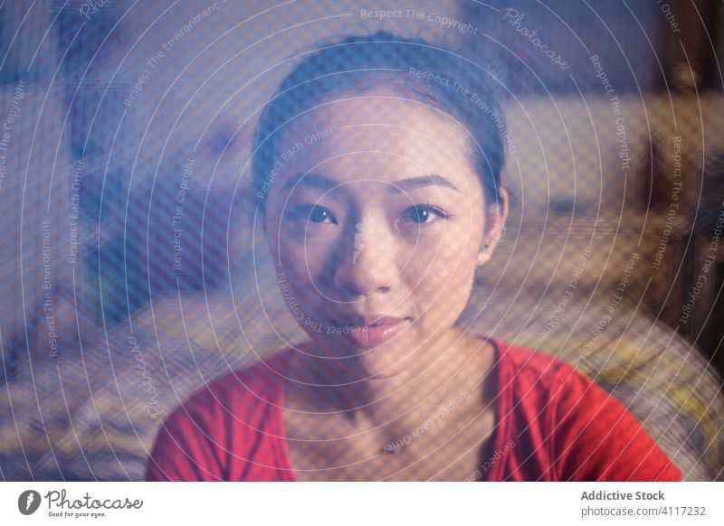 Asiatische Frau schaut durch ein Netz in die Kamera heimwärts Material gemütlich Raum versammeln Möbel untersuchen ethnisch blau Gewebe Stoff Detailaufnahme
