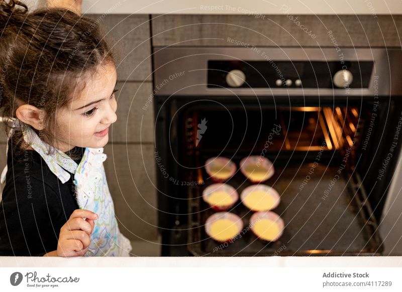 Niedliches Mädchen bei der Zubereitung von Cupcakes zu Hause Koch Ofen Küche heimwärts Lächeln ethnisch backen Wochenende Kind modern Schürze Dessert Glück