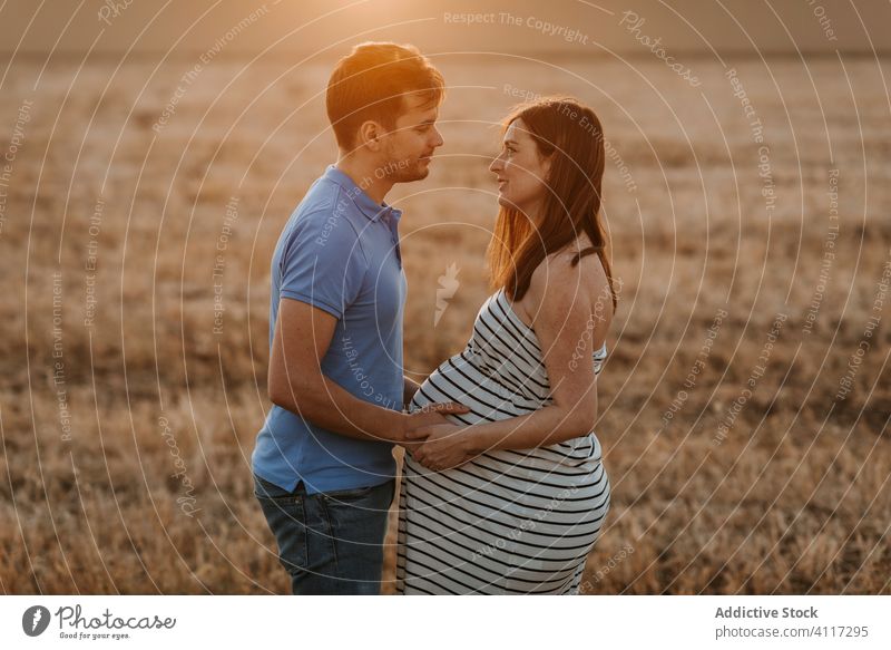 Paar wartet auf ein Baby im Feld schwanger Heufeld Sonnenuntergang Liebe berühren Bauch Zusammensein Angebot Landschaft Mann Frau Natur erwarten Partnerschaft