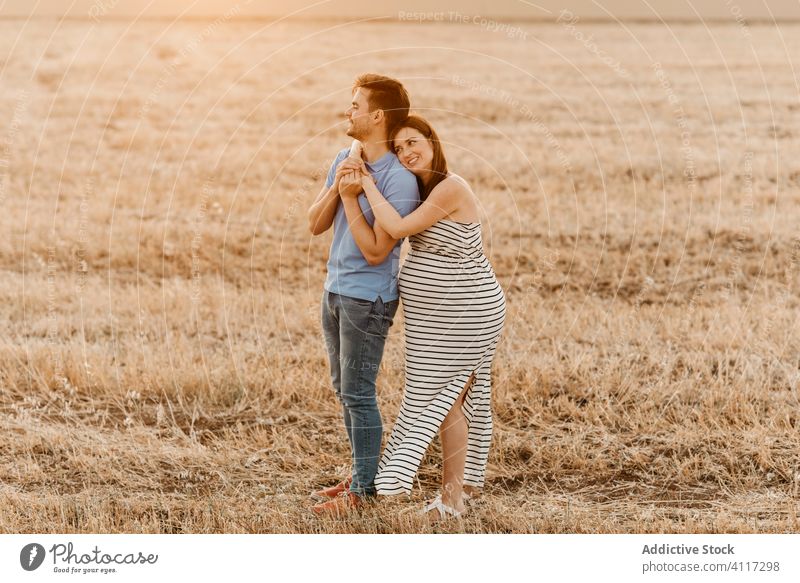 Paar wartet auf Baby, das sich im Feld umarmt schwanger Heufeld Sonnenuntergang Liebe berühren Bauch Zusammensein Angebot Landschaft Mann Frau Natur erwarten