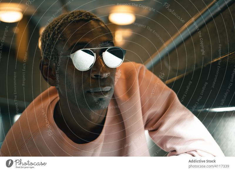Trendiger schwarzer Mann in beleuchtetem Gang Stil Stollen modern urban leuchten ethnisch selbstbewusst Outfit fettarm männlich Wand Sonnenbrille Sweatshirt