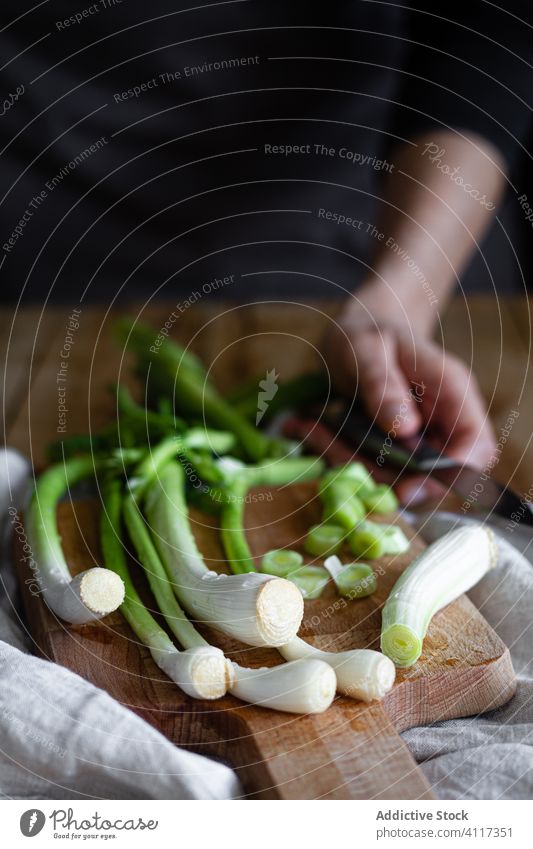 Anonyme Person mit frischen Frühlingszwiebeln auf dem Schneidebrett Serviette Tisch rustikal Küche reif Stoff Zusammensetzung Haufen hölzern Gemüse Lebensmittel