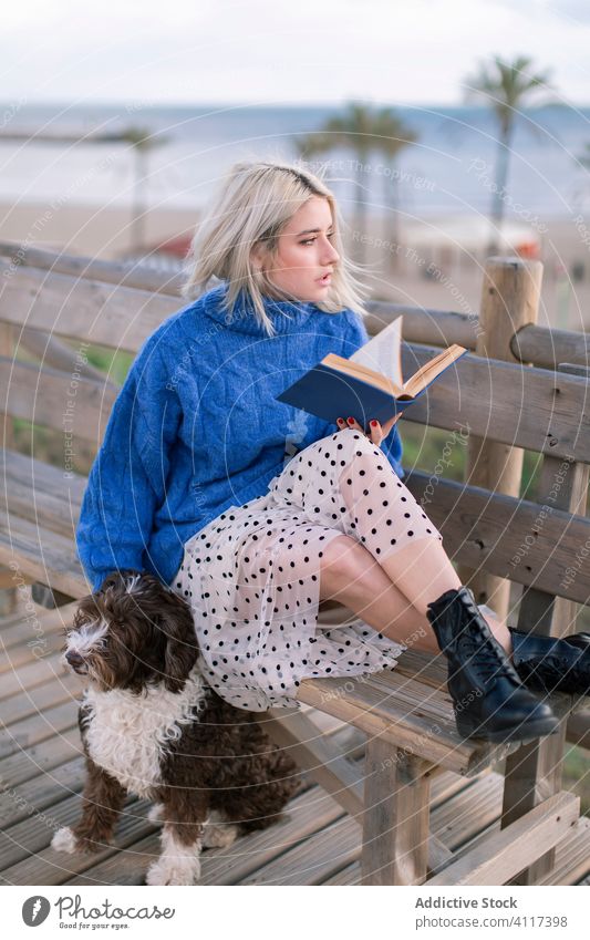 Junge Frau mit Hund liest Buch am Strand ruhen Seeküste Bank Terrasse lesen Zusammensein MEER Freund Haustier jung hölzern sich[Akk] entspannen Tier Stil trendy