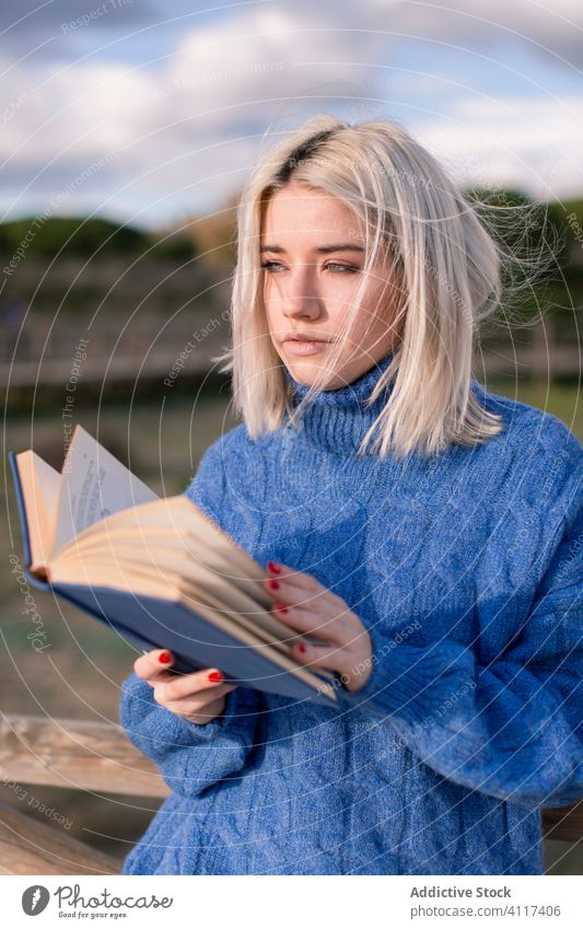 Nachdenkliche Frau, die ein Buch in der Natur liest lesen Landschaft Pullover genießen jung lässig blond ruhen Literatur Hobby Glück charmant Stil blau warm