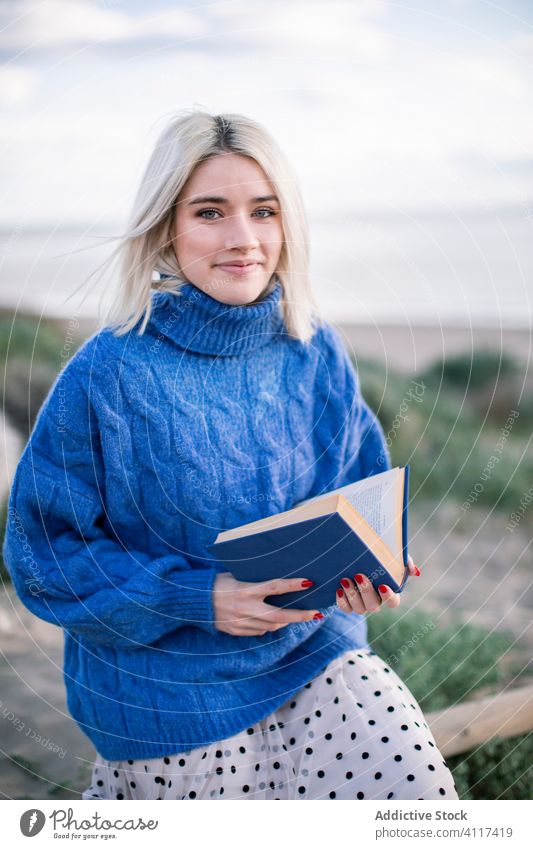 Frau genießt Buch auf dem Land und schaut in die Kamera lesen Glück heiter Natur Landschaft Pullover genießen jung lässig blond ruhen Literatur Hobby Lächeln