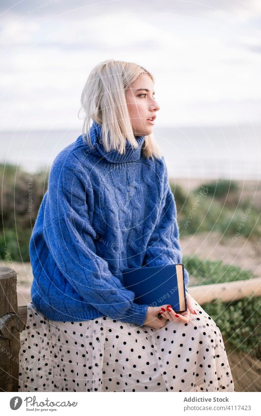 Nachdenkliche Frau, die ein Buch in der Natur liest lesen Landschaft Pullover genießen jung lässig blond ruhen Literatur Hobby Glück charmant Stil blau warm