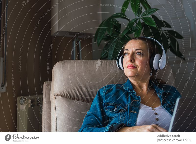 Erwachsener Freiberufler mit Laptop Frau freiberuflich Musik zuhören Kopfhörer benutzend heimwärts reif Fenster Armsessel sitzen Gerät Apparatur Drahtlos modern