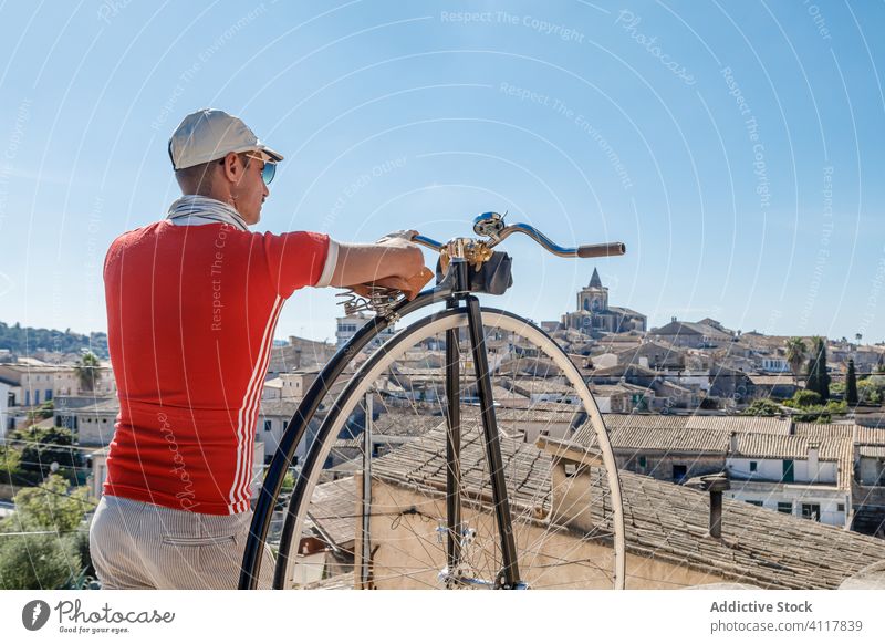 Männlicher Tourist mit Retro-Hochrad auf einem Aussichtspunkt vor der Kulisse einer alten Stadt Mann Fahrrad gealtert Tourismus Sightseeing Straße reisen antik