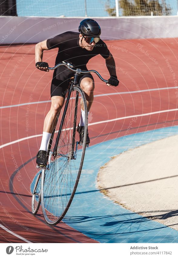 Entschlossener Sportler fährt mit einem Hochrad, während er allein im Sportstadion trainiert Fahrrad Mitfahrgelegenheit Stadion Radfahrer Athlet Pfennigfuchser