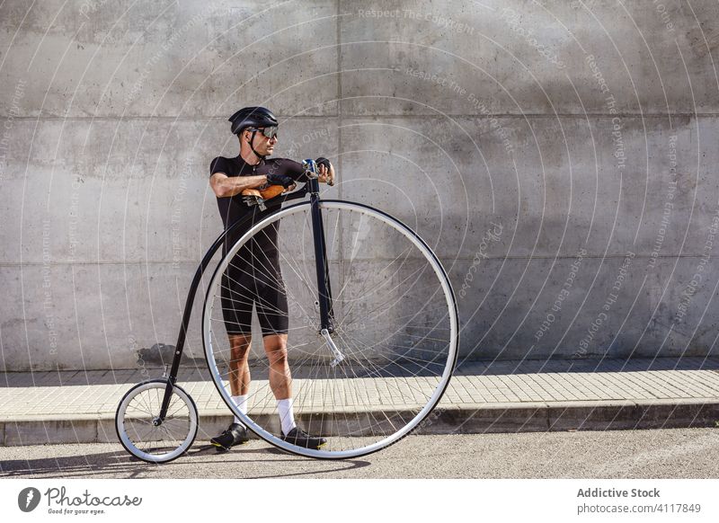 Erwachsener Sportler mit Retro-Groschenrad auf der Straße in der Stadt Fahrrad Radfahrer Pfennigfuchser Mann Hochrad Reiter Athlet urban sportlich Bestimmen Sie