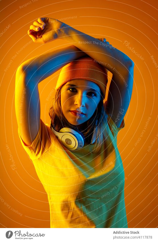 Frauenmodell mit Kopfhörern um den Hals Stil modern leuchten hell Hände hinter dem Kopf jung Model Accessoire Hut T-Shirt Hipster selbstbewusst Kopfbedeckung