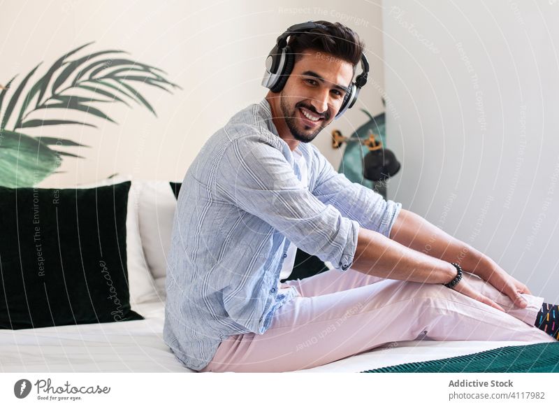 Ethnischer Mann beim Musikhören auf dem Bett zuhören heimwärts Kopfhörer ethnisch gemütlich genießen Wochenende männlich sitzen Komfort Melodie Audio Gesang