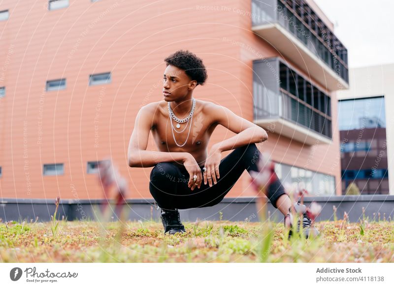 Ethnisches männliches Modell ohne Hemd mit Halsketten auf der Straße sitzend Mann trendy anketten cool unabhängig Streetstyle jung selbstbewusst modern schwarz