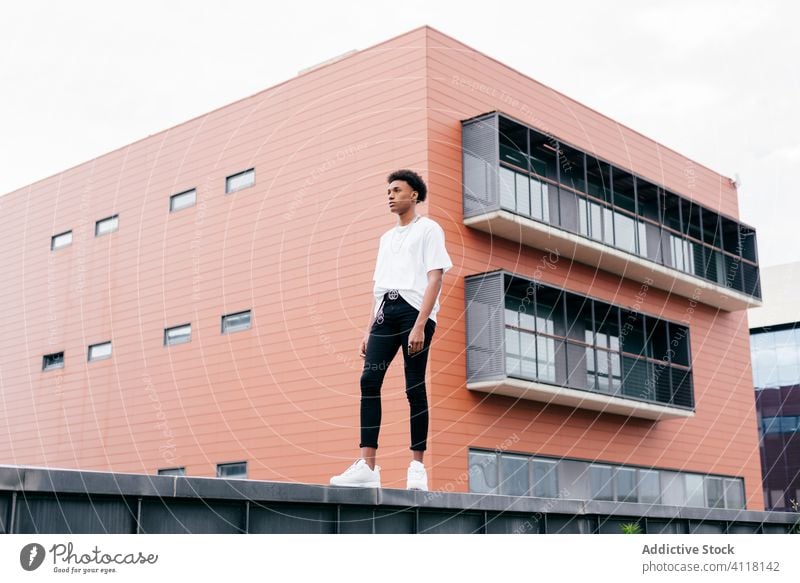 Modischer ethnischer Mann stellt sich gegen modernes Bauen Streetstyle Mode trendy cool urban Gebäude jung Großstadt selbstbewusst Afroamerikaner schwarz