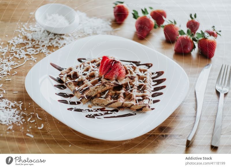 Waffeln und Erdbeeren mit Schokoladenüberzug und Kokosnussflocken Belag Schuppen Frühstück Teller Silberwaren Tisch weich süß lecker Saucen hölzern Dessert