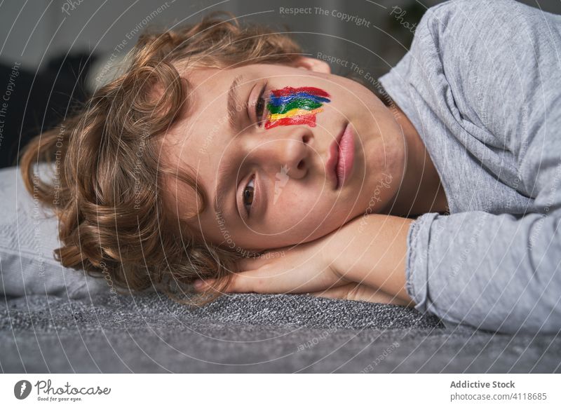 Junge mit Regenbogen im Gesicht auf dem Boden liegend heimwärts Quarantäne Konzept Symbol Lügen Stock Decke Kopfkissen Kind Pandemie Seuche ruhen