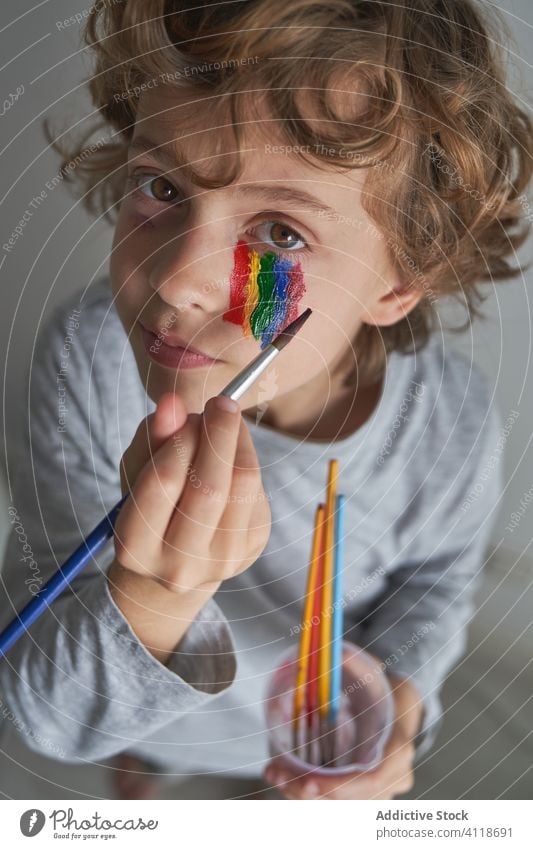 Junge malt Regenbogen auf Gesicht heimwärts Quarantäne Farbe Konzept Bürste Symbol Kind Pandemie Seuche ruhen sich[Akk] entspannen Isolation bezaubernd niedlich