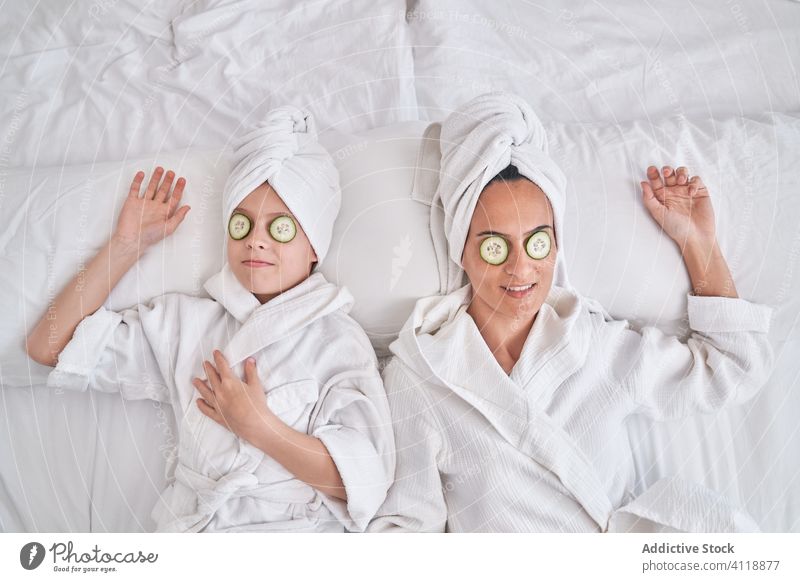 Fröhliche Frau mit Kind genießt Wellnessbehandlung zu Hause Schönheit Hautpflege Salatgurke Mundschutz Mutter Zusammensein Spaß haben genießen Lachen ruhen