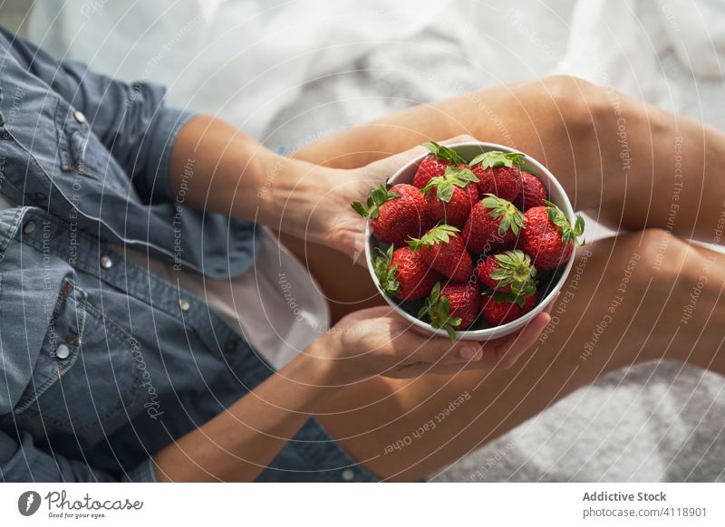 Crop-Frau mit Erdbeeren auf dem Bett sitzend Schalen & Schüsseln heimwärts zeigen Sommer Wochenende reif ruhen Lebensmittel Frucht Beeren Dessert Morgen Decke