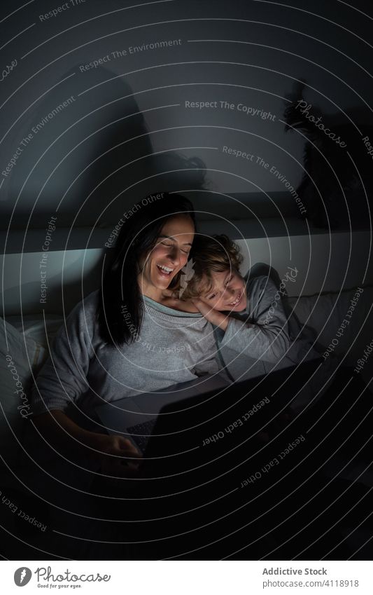 Fröhliche Mutter und Sohn mit Laptop im Bett heimwärts Nacht Zusammensein zuschauen Film Lächeln dunkel benutzend Schlafzimmer Frau Junge Kind Lügen Gerät