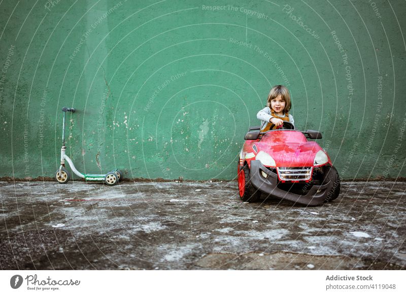 Kleines Mädchen fährt Elektroauto Laufwerk PKW elektrisch Spielzeug spielen schäbig Wand gebrochen Stoßstange lässig niedlich wenig Kind verwittert Schaden rau