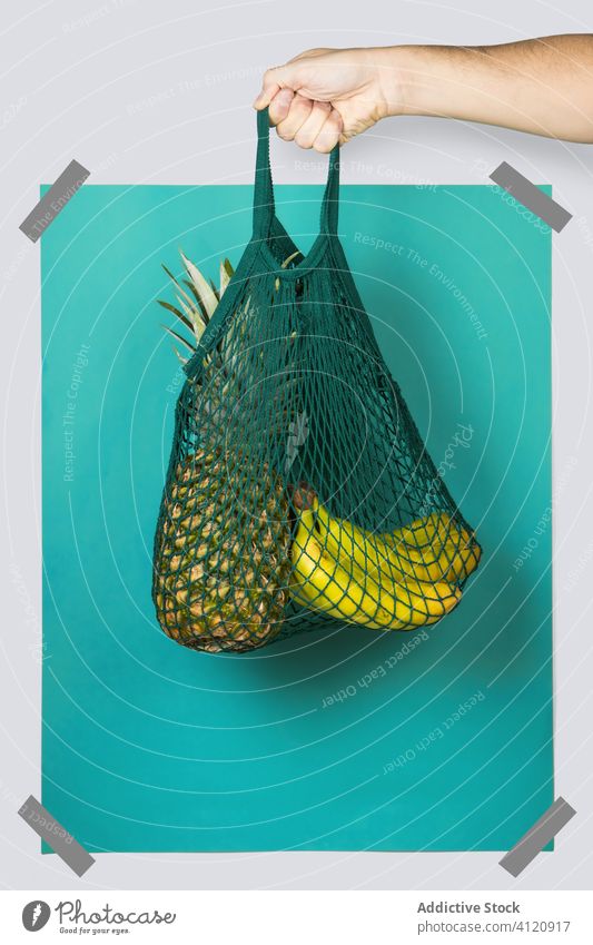 Crop Person trägt String Tasche mit Ananas und Bananen keine Verschwendung Lebensmittelgeschäft Konzept umweltfreundlich führen Rechteck hell farbenfroh