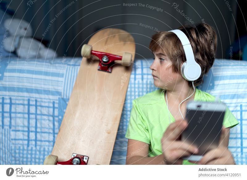 Fröhliches Kind mit Kopfhörern, das zu Hause sein Smartphone benutzt Apparatur heimwärts Junge benutzend Talkrunde Gerät online zuhören Internet Glück Lifestyle