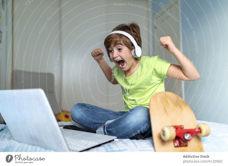 Aufgeregter Junge, der das Spiel auf seinem Laptop verfolgt Kind feiern aufgeregt Schlafzimmer gewinnen benutzend heimwärts Sieg Triumph Streichholz Bett