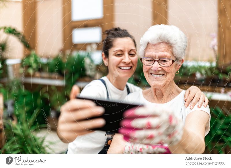 Fröhliche Gärtnerinnen machen ein Selfie Frauen Umarmung Gewächshaus Smartphone Lächeln Erwachsener Senior Kollege Arbeit Glück heiter Gerät Apparatur
