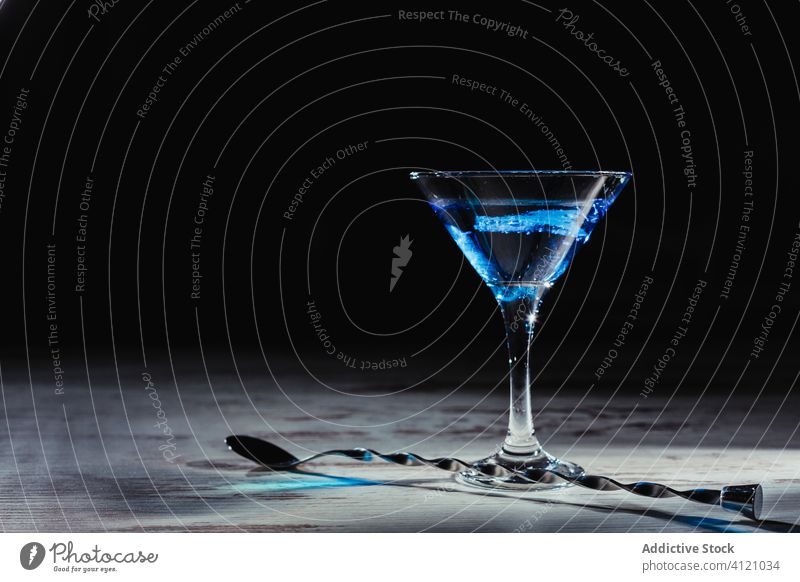Lebendiges blaues Cocktailglas und gedrehter Löffel auf rustikalem Tisch trinken Alkohol Eis schäbig Getränk dunkel Glas lang Martini feiern hölzern Rochen