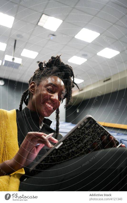Fröhlicher afroamerikanischer Student, der in der Aula ein Tablet betrachtet Frau Schüler benutzend Tablette dozieren Saal Lächeln lernen ethnisch modern
