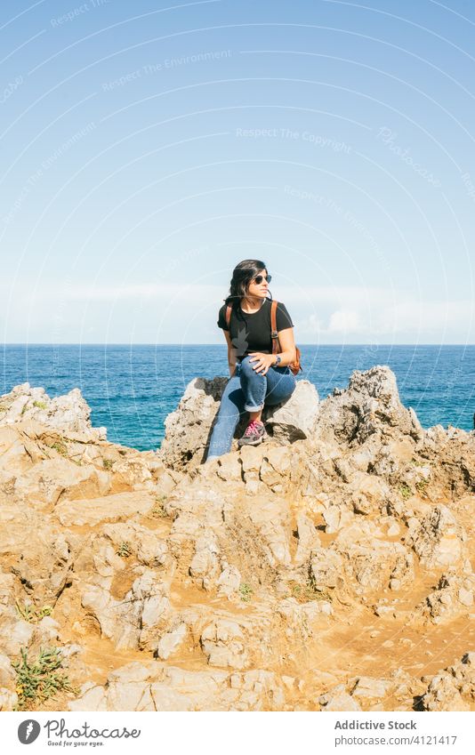 Junge Frau sitzt auf einer Klippe am Meer Meeresufer Strand MEER Harmonie erstaunlich Windstille Himmel Ansicht idyllisch Felsen reisen schön Sonnenbrille Natur