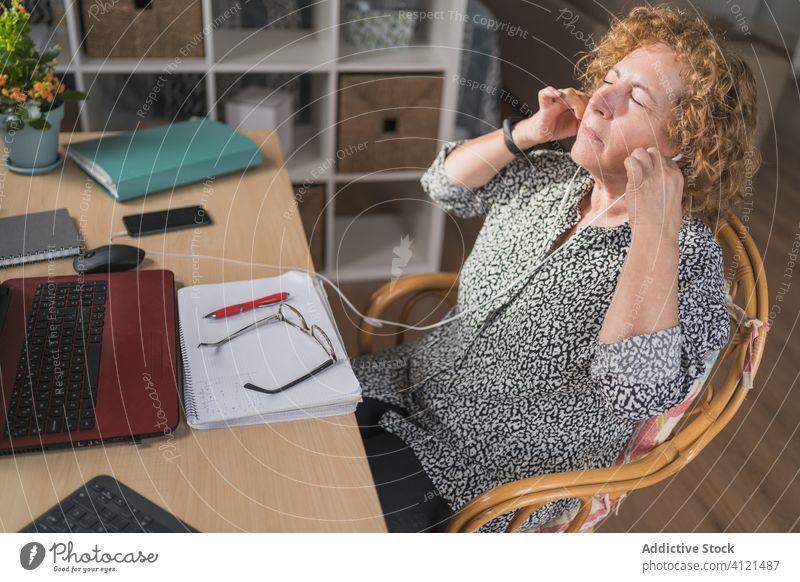 Nachdenkliche erwachsene Frau, die Musik über Kopfhörer hört, während sie zu Hause am Laptop arbeitet ruhen heimwärts Entfernung Arbeit abgelegen Pause genießen