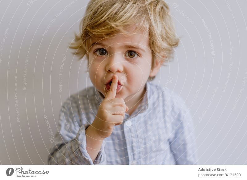 Anbetungswürdiger Junge mit Schweigegeste Stille gestikulieren bezaubernd Zeigefinger wenig niedlich Kind Inhalt Kindheit lässig Gesichtsausdruck Glück stehen
