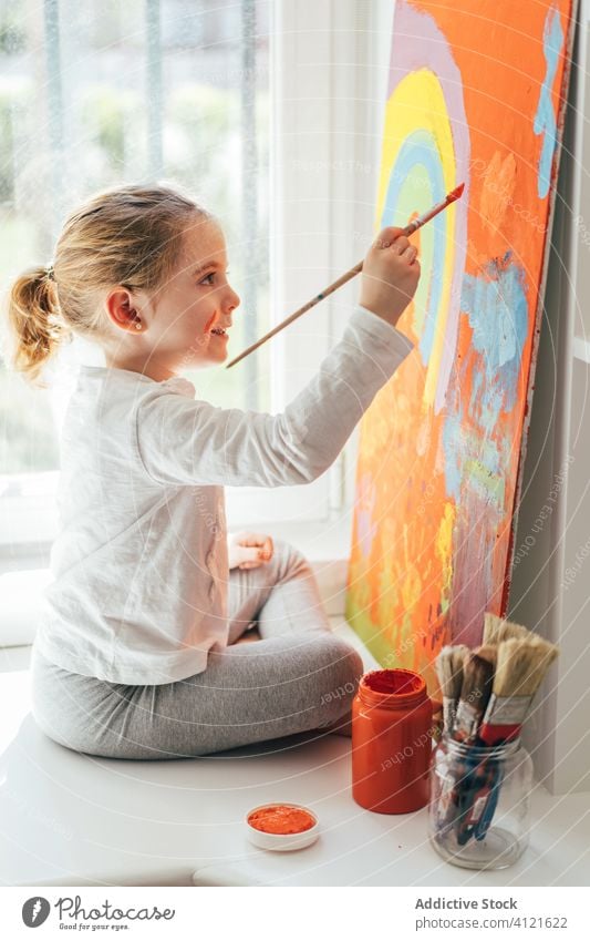 Kleines Mädchen malt Bild mit Pinsel Leinwand zeichnen Farbe Pinselblume Regenbogen Malerei kreativ farbenfroh orange Fensterbrett lässig Kunst Hobby