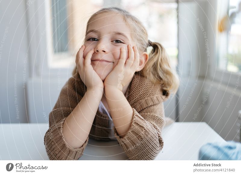 Glückliches kleines Mädchen schaut in die Kamera in einem gemütlichen Haus Lächeln heimwärts Kindergarten sich auf die Hand lehnen charmant Porträt niedlich