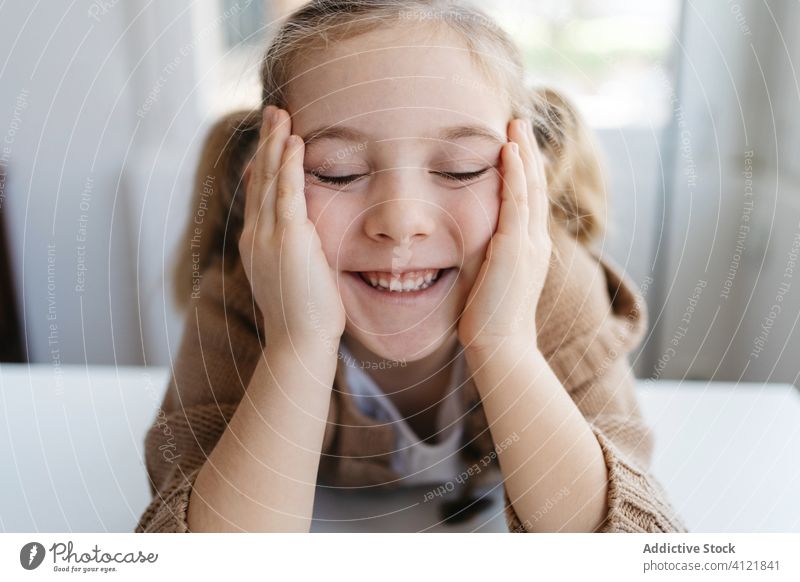 Glückliches kleines Mädchen mit geschlossenen Augen in einem gemütlichen Haus Lächeln heimwärts Kindergarten sich auf die Hand lehnen geschlossene Augen