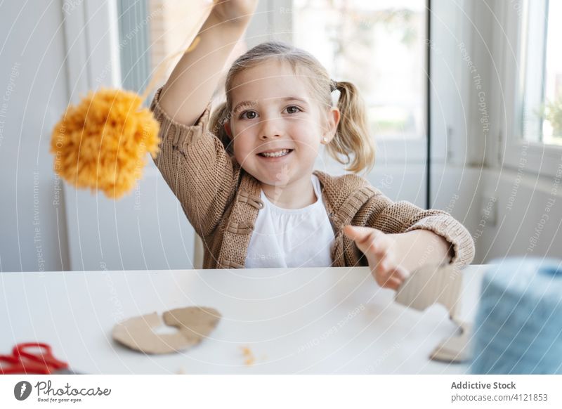 Fröhliches kleines Kind, das mit weichem Kunsthandwerk im hellen Haus spielt heiter Mädchen Pompom Glück spielen Basteln handgefertigt heimwärts Pompons
