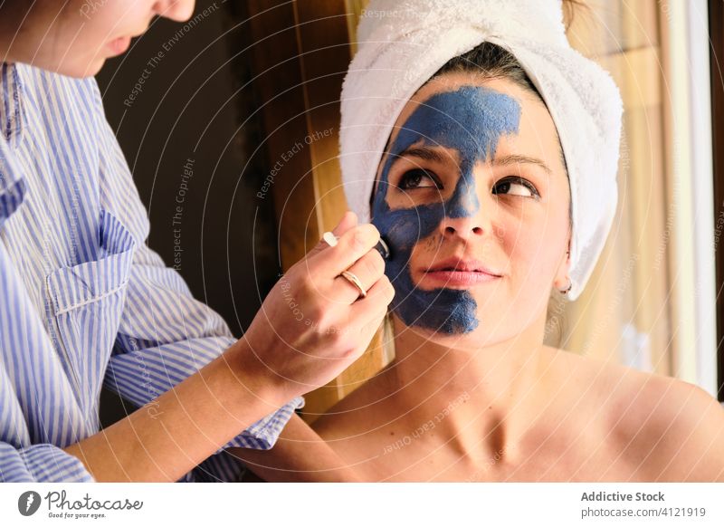 Unbekannte Frau trägt Tonmaske auf das Gesicht einer glücklichen Frau auf Frauen bewerben heimwärts Pflege Hautpflege Gelassenheit zufrieden Glück Zusammensein