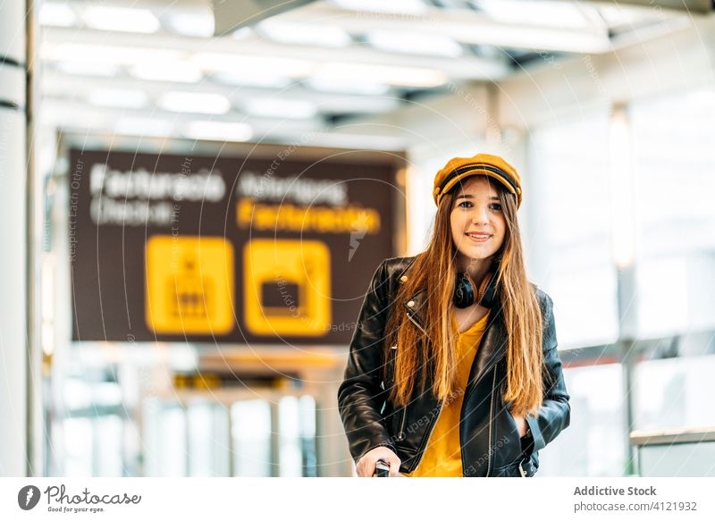 Trendige junge Frau im modernen Flughafenterminal Tourist trendy Passagier heiter Terminal Kopfhörer Stil Mode Abheben Lächeln Ausflug Handgriff warten schwarz