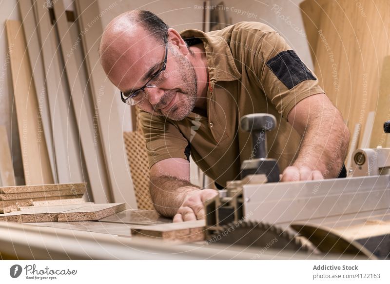 Fleißiger Holzarbeiter beim Schneiden von Holz mit einer Fräsmaschine im Arbeitsraum Arbeitsplatz Maschine Schreinerei entgittern messen achtsam Mann Säge