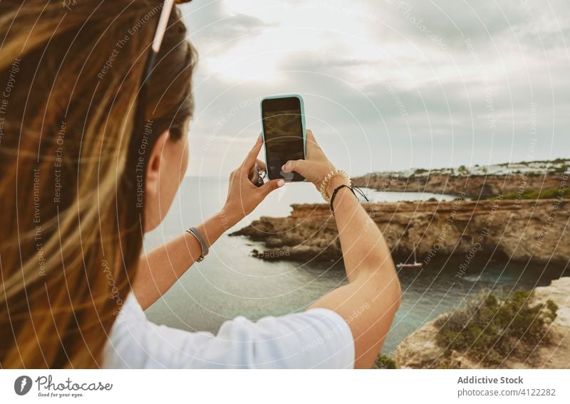Anonyme Touristin, die mit ihrem Smartphone ein Foto von der felsigen Küste Ibizas macht Frau fotografieren Meeresufer wolkig Natur Klippe Reise Felsen Spanien
