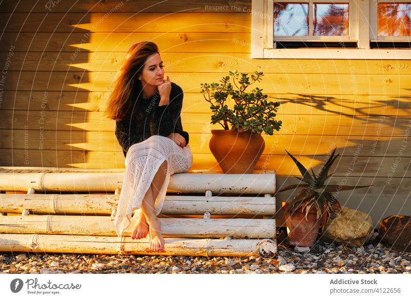 Gelassene Frau entspannt sich auf einer Bank in der Nähe des Hauses sich[Akk] entspannen Sonnenuntergang Gelassenheit Barfuß hölzern Kälte Wochenende Landschaft
