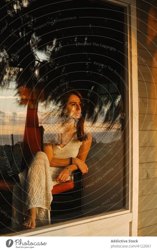 Ruhige Frau im Sessel entspannt am Fenster sich[Akk] entspannen bewundern Sonnenuntergang Armsessel Sommer Urlaub genießen Gelassenheit malerisch Haus Freude