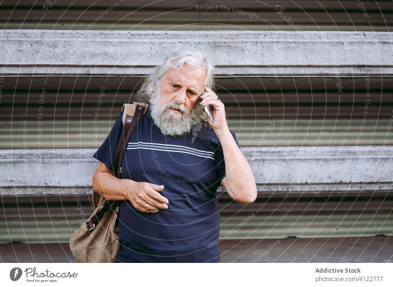 Älterer Reisender mit Smartphone auf der Straße gealtert Mann Suche Information Großstadt Funktelefon benutzend männlich Tourist älter lange Haare graues Haar