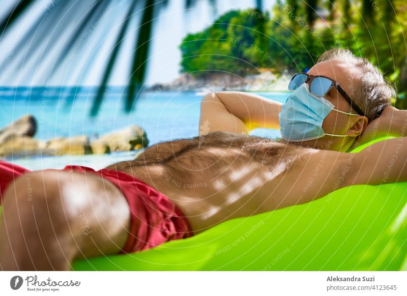 Reifer Mann in Schutzmaske und Sonnenbrille entspannt am Strand. Exotische Tropenlandschaft mit türkisfarbenem Wasser und Palmen. Tourismus während der Pandemie. Sicheres Reisen.