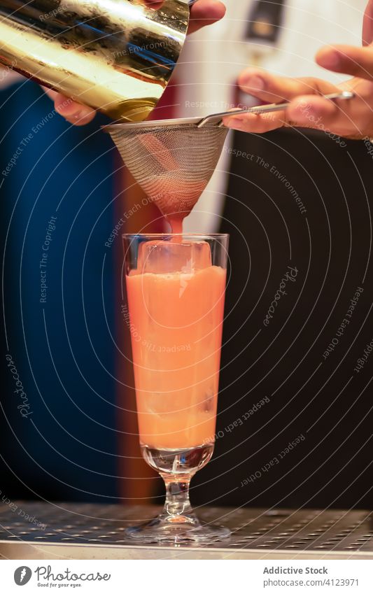 Barkeeper mit Sieb beim Einschenken eines Cocktails in ein Glas vorbereiten trinken Alkohol frisch Eis Barmann eingießen orange Hand Abfertigungsschalter